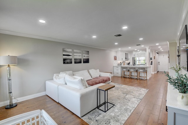 living area with visible vents, crown molding, baseboards, light wood finished floors, and recessed lighting