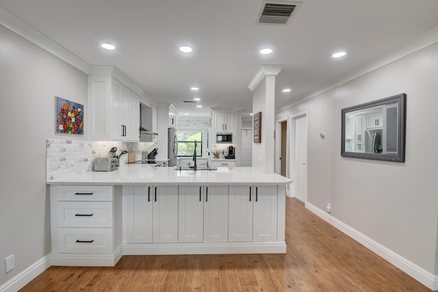 kitchen with built in microwave, light countertops, a peninsula, stainless steel fridge, and white cabinetry