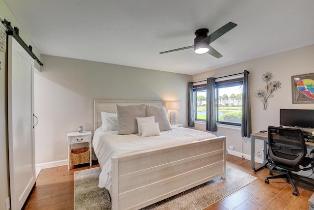 bedroom with a ceiling fan, baseboards, a barn door, and light wood-style flooring