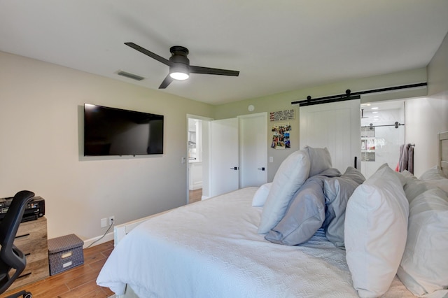 bedroom featuring ceiling fan, a barn door, baseboards, light wood-type flooring, and visible vents