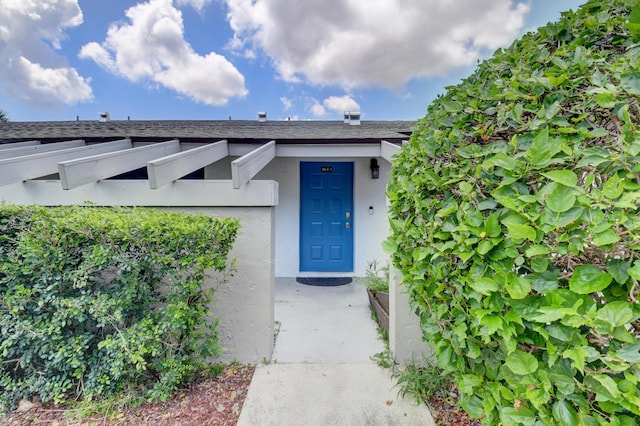 property entrance featuring roof with shingles and stucco siding