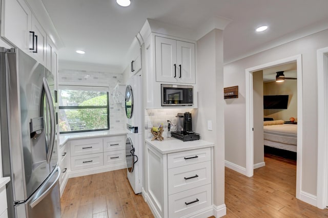 kitchen with light countertops, stainless steel appliances, stacked washer / dryer, and light wood-type flooring