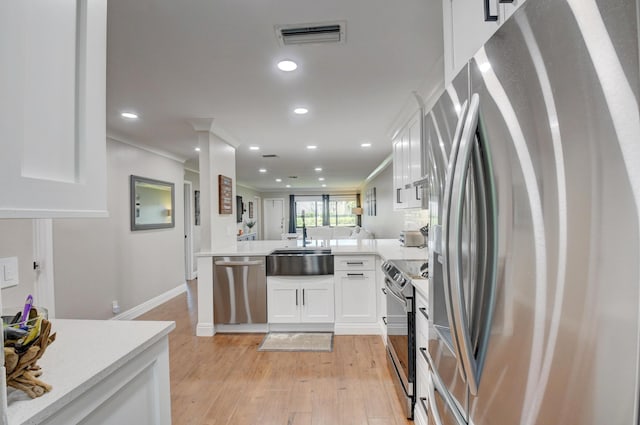 kitchen featuring visible vents, crown molding, a peninsula, white cabinetry, and stainless steel appliances