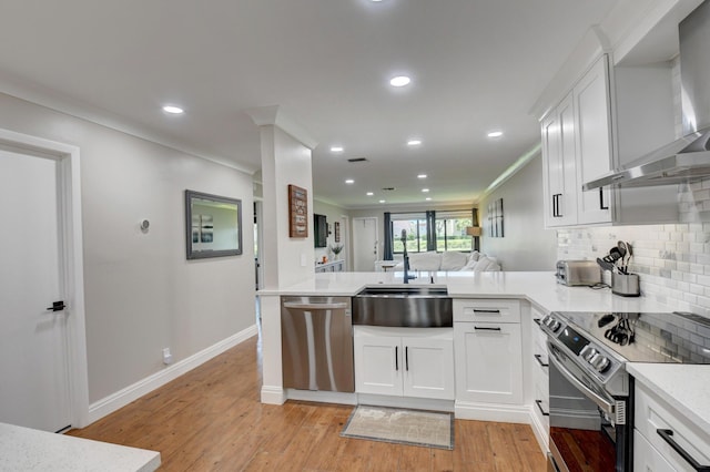 kitchen featuring decorative backsplash, a peninsula, wall chimney exhaust hood, light wood-style flooring, and appliances with stainless steel finishes