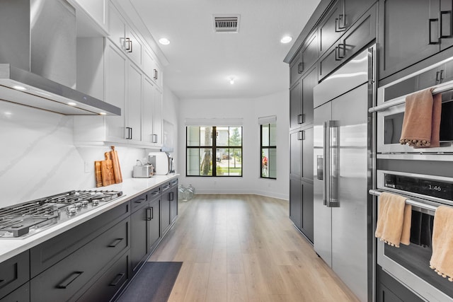 13158 Artisan Cir, Palm Beach Gardens, FL 33418 - kitchen featuring wall chimney exhaust hood, appliances with stainless steel finishes, white cabinets, light wood-type flooring, and baseboards