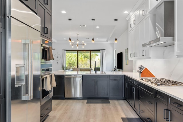 13158 Artisan Cir, Palm Beach Gardens, FL 33418 - kitchen featuring stainless steel appliances, wall chimney range hood, a sink, light wood-style floors, and white cabinets