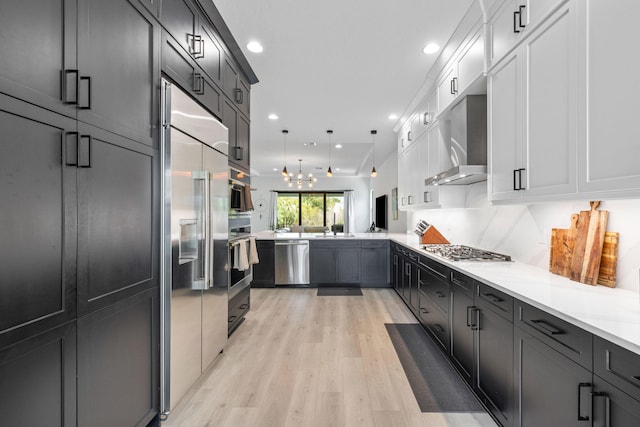 13158 Artisan Cir, Palm Beach Gardens, FL 33418 - kitchen featuring appliances with stainless steel finishes, wall chimney range hood, a peninsula, light countertops, and light wood-type flooring