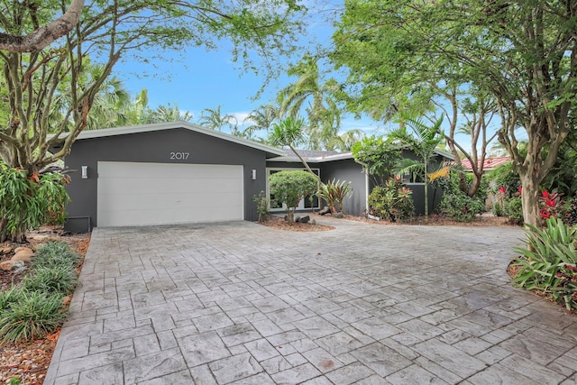 ranch-style home featuring an attached garage, decorative driveway, and stucco siding