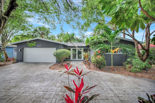 view of front facade featuring decorative driveway, a garage, french doors, and stucco siding