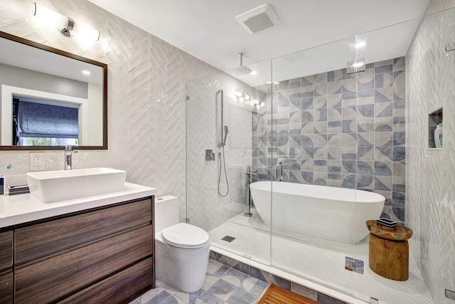 bathroom with a walk in shower, a freestanding bath, vanity, tile walls, and visible vents