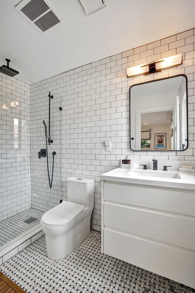 bathroom featuring visible vents, vanity, toilet, tile walls, and tiled shower