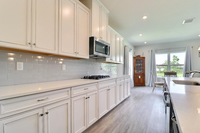 kitchen with a sink, light countertops, light wood-style flooring, stainless steel microwave, and decorative backsplash