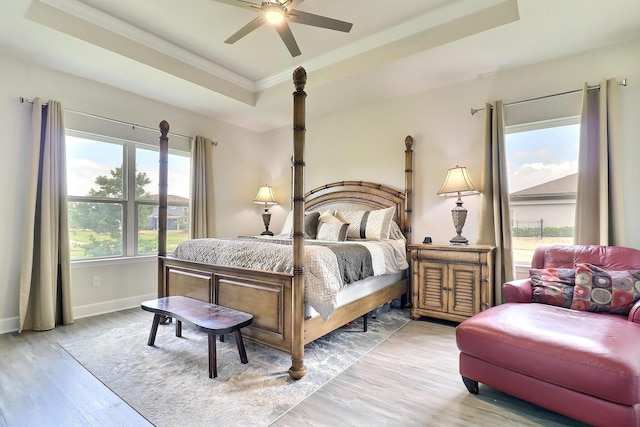 bedroom featuring crown molding, ceiling fan, a raised ceiling, light wood-style flooring, and baseboards