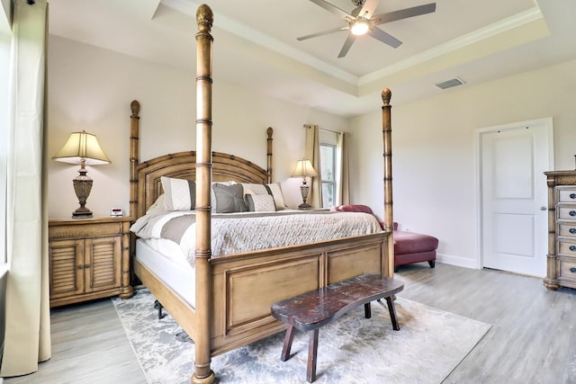 bedroom featuring visible vents, crown molding, light wood-style floors, baseboards, and a tray ceiling