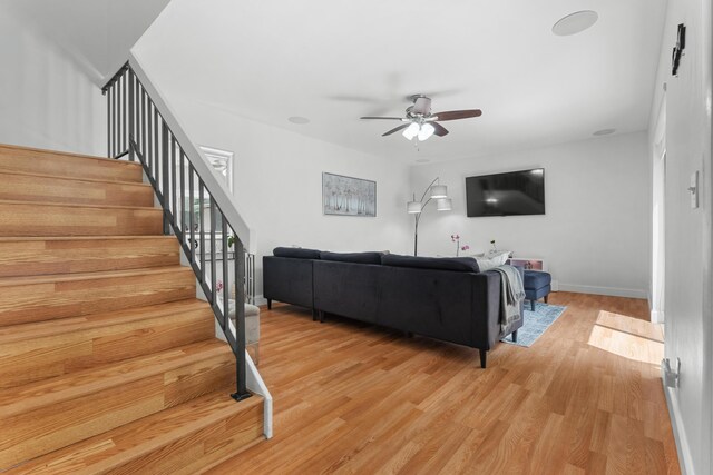 living area featuring a ceiling fan, baseboards, stairway, and light wood-style floors