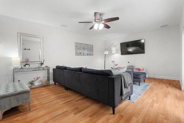 living room featuring baseboards, a ceiling fan, and light wood-style flooring