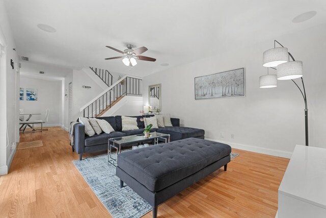 living area with light wood-style floors, a ceiling fan, baseboards, visible vents, and stairway