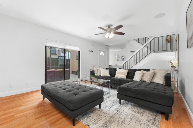 living area with a ceiling fan, baseboards, light wood-style flooring, and stairway