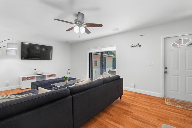 living room featuring baseboards, ceiling fan, and light wood finished floors