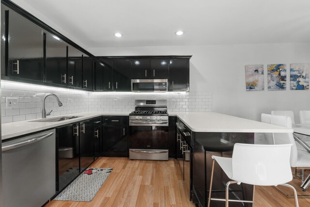 kitchen featuring dark cabinets, a sink, appliances with stainless steel finishes, and a peninsula