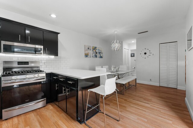 kitchen featuring decorative backsplash, a peninsula, light countertops, dark cabinetry, and stainless steel appliances