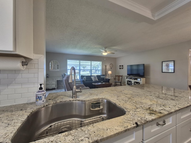 kitchen featuring a ceiling fan, light stone countertops, open floor plan, white cabinets, and a sink