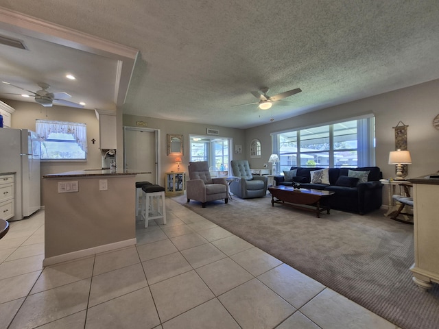 living room featuring light colored carpet, a ceiling fan, light tile patterned floors, and a healthy amount of sunlight