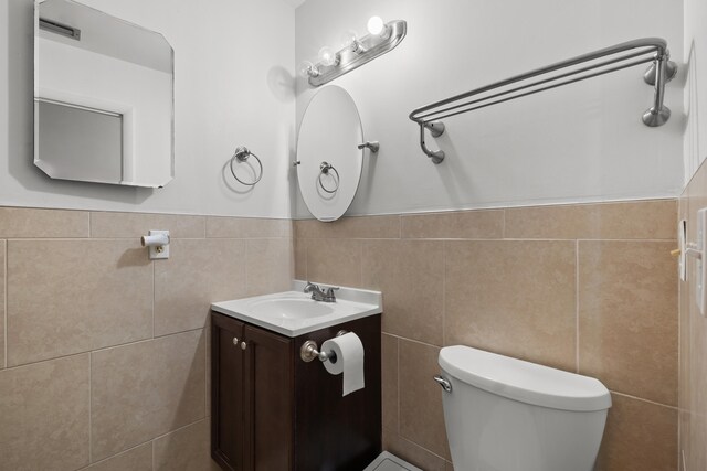 115 NE Caprona Ave, Port Saint Lucie, FL 34983 - half bathroom featuring tile walls, toilet, vanity, and a wainscoted wall