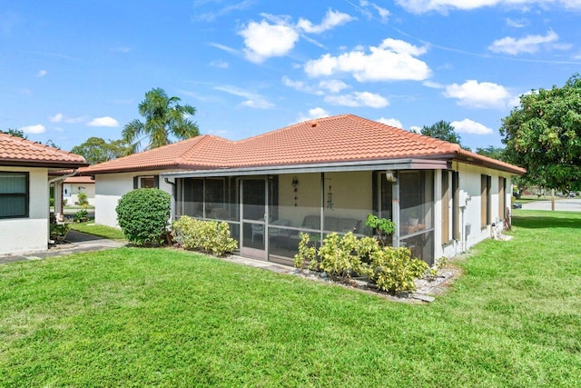 back of property with a lawn, stucco siding, a sunroom, and a tile roof