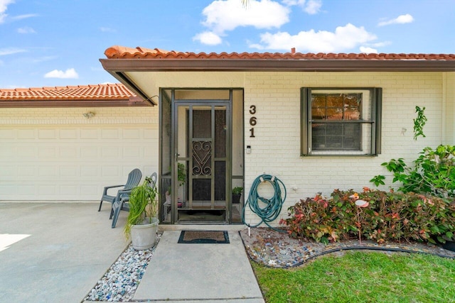 doorway to property featuring an attached garage, driveway, and brick siding