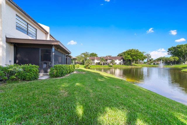view of grassy yard with a sunroom and a water view