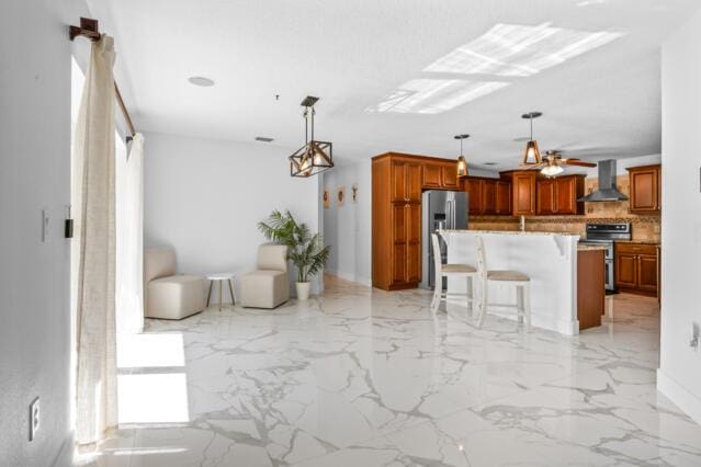 kitchen with wall chimney range hood, a breakfast bar area, marble finish floor, stainless steel appliances, and decorative backsplash