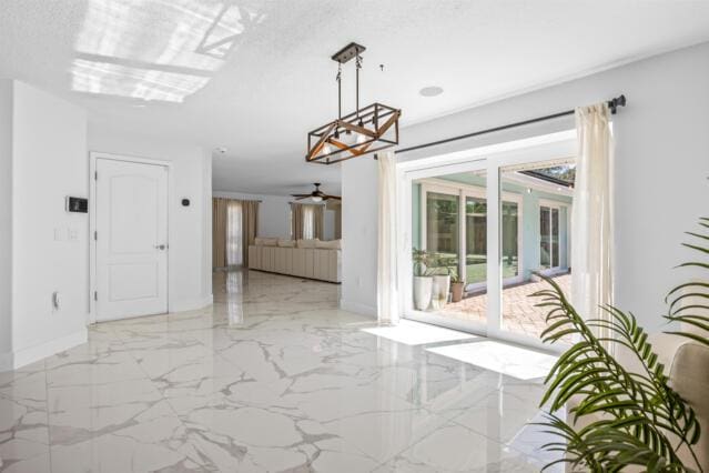 unfurnished dining area with baseboards, ceiling fan with notable chandelier, and marble finish floor