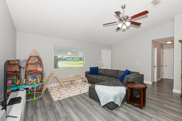 living room featuring a ceiling fan, vaulted ceiling, wood finished floors, and visible vents