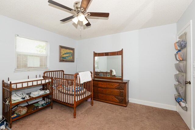 carpeted bedroom featuring a ceiling fan and a nursery area