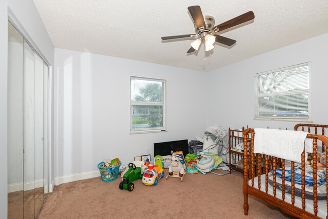 carpeted bedroom with baseboards, a ceiling fan, a closet, and a textured ceiling