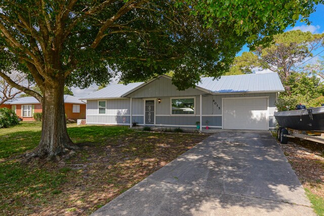 ranch-style home featuring board and batten siding, metal roof, a front yard, concrete driveway, and an attached garage