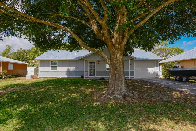 ranch-style home with a garage, metal roof, concrete driveway, and a front lawn
