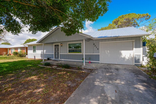 ranch-style home with board and batten siding, metal roof, a front yard, a garage, and concrete driveway