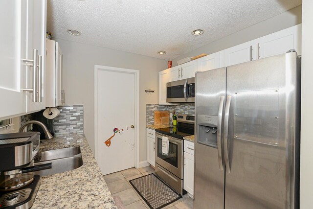 kitchen with appliances with stainless steel finishes, a sink, a textured ceiling, white cabinetry, and tasteful backsplash