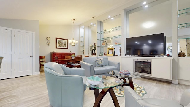 living area with a glass covered fireplace, vaulted ceiling, wood finished floors, and a notable chandelier