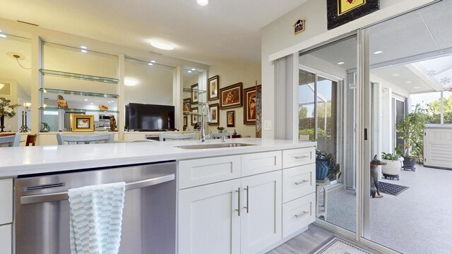 kitchen with stainless steel dishwasher, white cabinets, open floor plan, and a sink