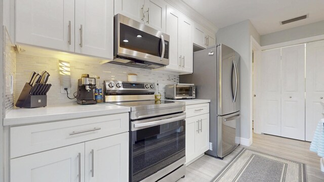 kitchen featuring backsplash, appliances with stainless steel finishes, a toaster, light countertops, and white cabinets