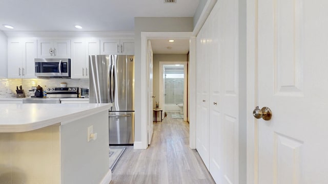 kitchen featuring appliances with stainless steel finishes, tasteful backsplash, light countertops, light wood finished floors, and white cabinetry