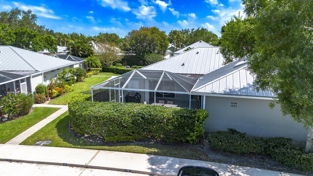 rear view of house with a standing seam roof, a lanai, metal roof, a lawn, and stucco siding