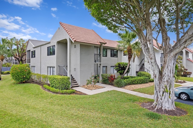 view of front facade featuring stairs, a front lawn, stucco siding, and a tile roof