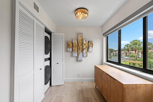 laundry area with an inviting chandelier, laundry area, stacked washer and dryer, baseboards, and light wood-style floors