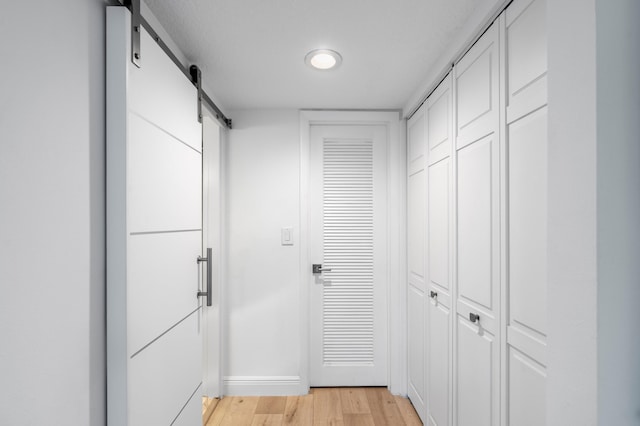 hall featuring baseboards, a barn door, and light wood-style flooring