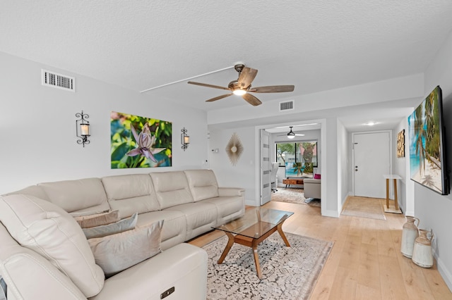 living room with visible vents, a ceiling fan, light wood finished floors, and a textured ceiling