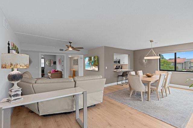 living room featuring baseboards, a ceiling fan, light wood-style flooring, and visible vents